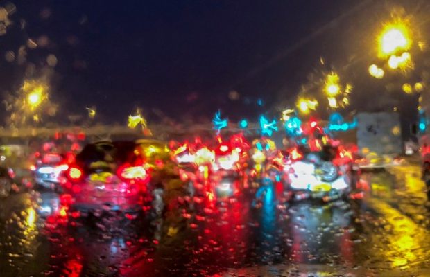 View through a wet car windscreen showing the blurred lights of vehicles and road side lights in front of the vehicle.