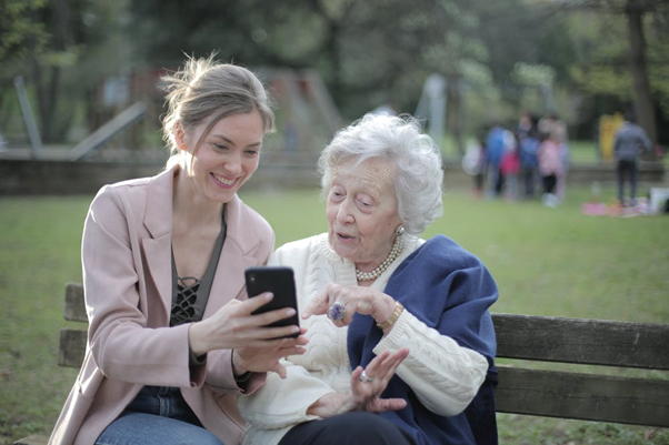 A young woman sat outside showing an older woman something on her smartphone.